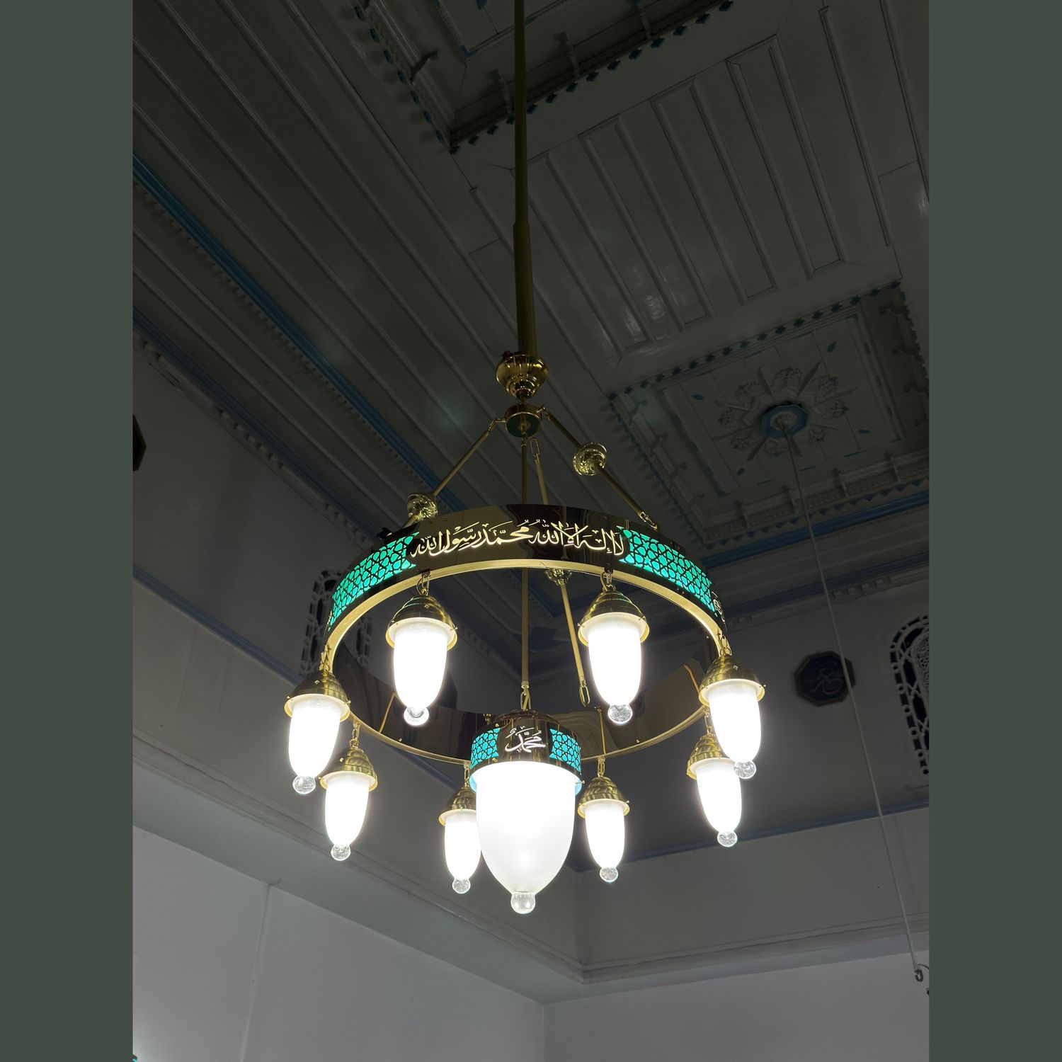Tek halkalı 80 cm turkuaz tevhidli ledli cami avizesi ahşap tavanlı mekânda, merkez sarkıtı görünür hâlde