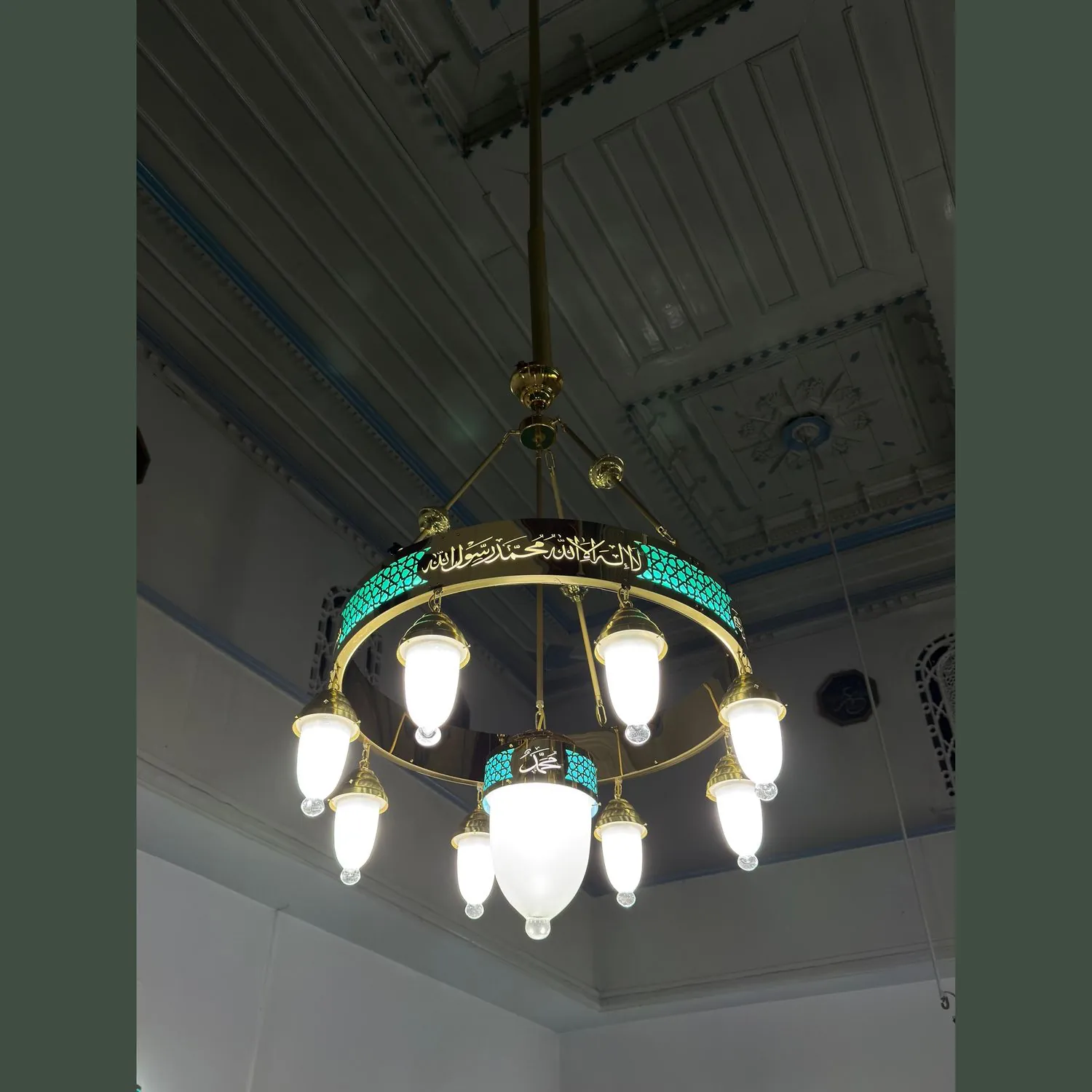 Tek halkalı 80 cm turkuaz tevhidli ledli cami avizesi ahşap tavanlı mekânda, merkez sarkıtı görünür hâlde