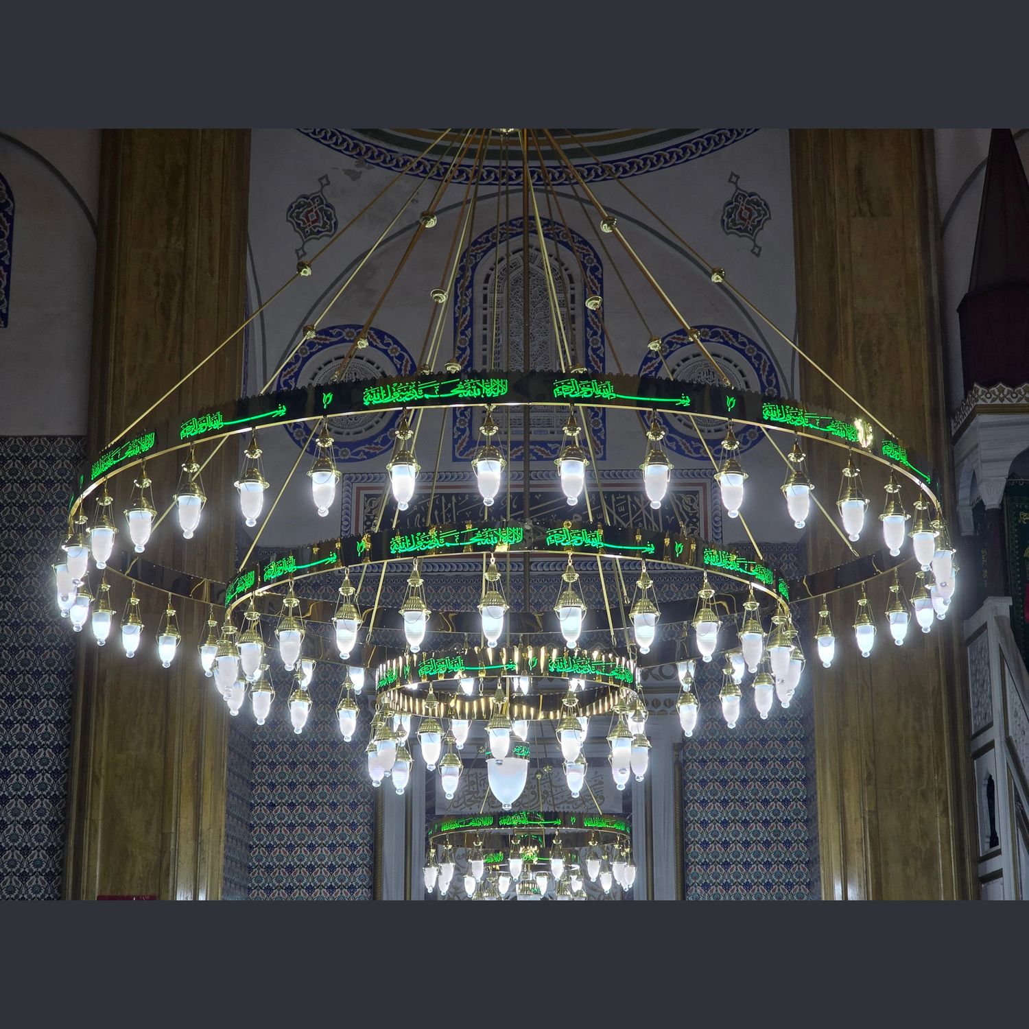 Dört kademeli yeşil tevhidli ledli cami avizesi cami içinde, çinili mihrabın önünde yanarken