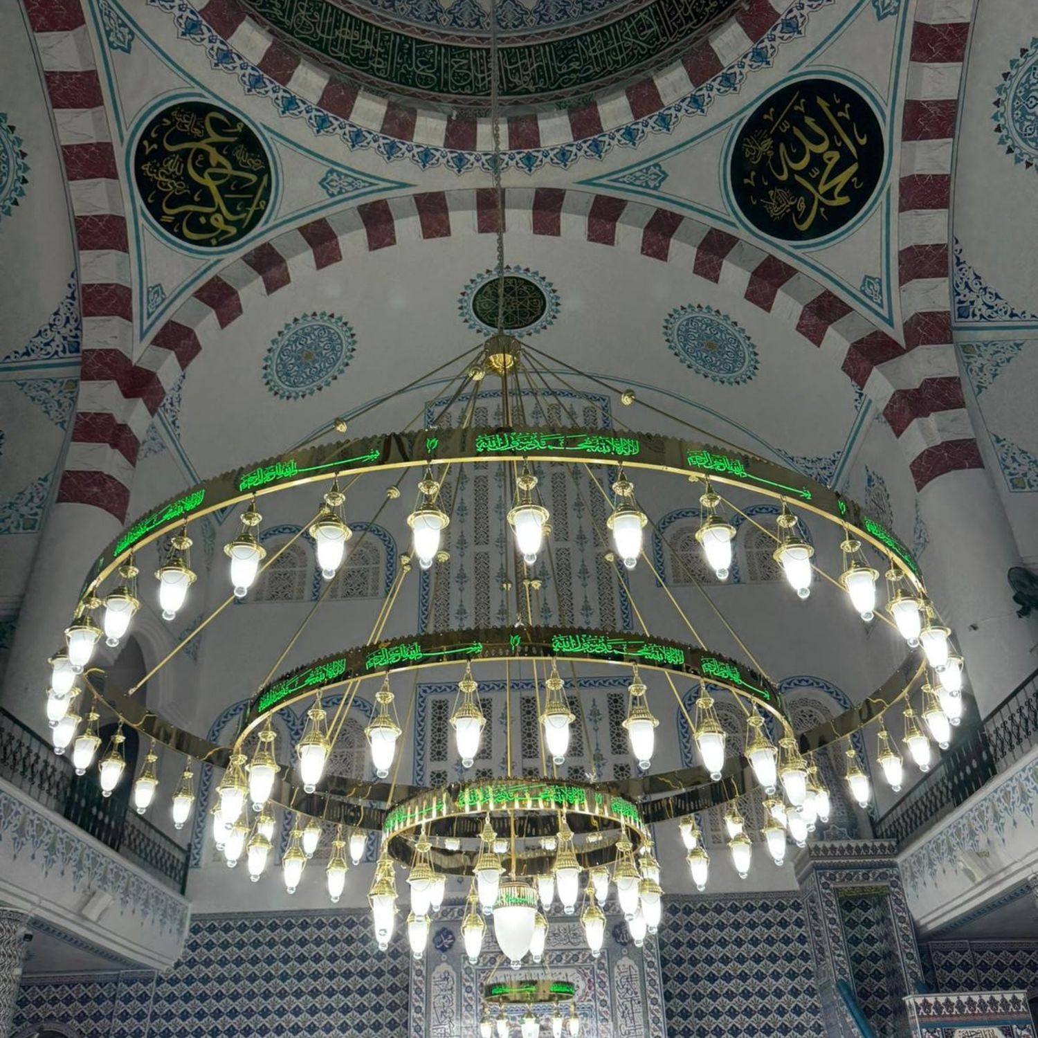 Üç kademeli yeşil tevhidli ledli cami avizesi cami içinde, çinili duvarların önünde yanarken
