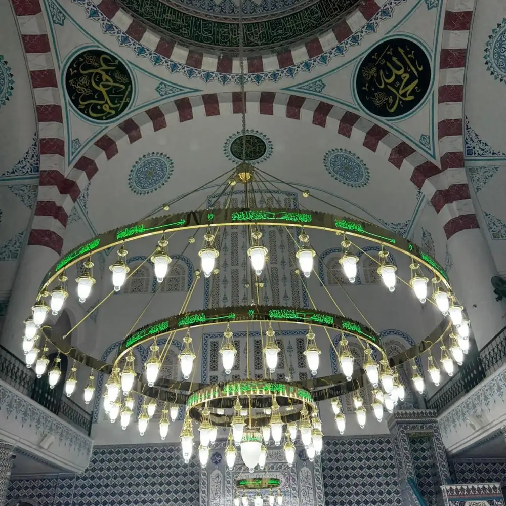 Üç kademeli yeşil tevhidli ledli cami avizesi cami içinde, çinili duvarların önünde yanarken